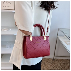 Detail of dark red quilted crossbody bag with woven handle and gold hardware shown on model