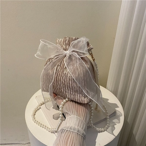 Elegant champagne bucket bag with white organza bow and pearl strap on display stand