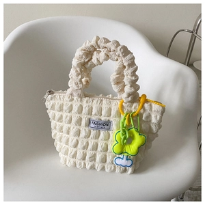 Detail of cream bubble textured handbag with fashion label and flower charm