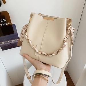 Minimalist beige bucket bag with decorative silk scarf and gold chain handle