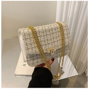 Detail of tweed crossbody bag featuring gold chain strap and metallic square lock closure