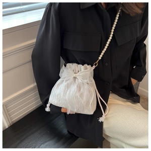 Detail of white pleated bucket bag with organza bow and long faux pearl shoulder strap