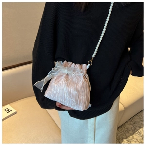 Detail of champagne pleated bucket bag with pearl chain and white ribbon on a model