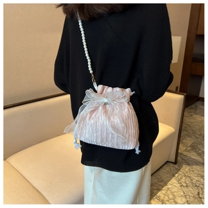 Rear view of a model wearing a pink pleated satin bucket bag with pearl strap and bow