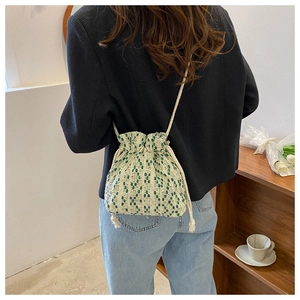 Detail of woven drawstring bucket bag in cream and green worn by a model in a casual setting