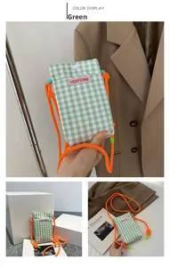 Detail der grünen karierten Handy-Umhängetasche mit orangefarbener Kordel und Druckknopf