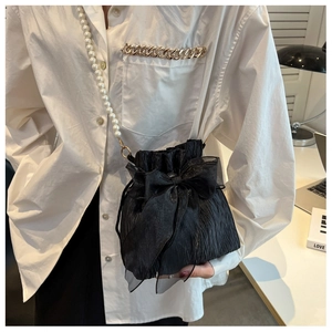 Detail of black pleated bucket bag featuring an organza bow and pearl shoulder strap