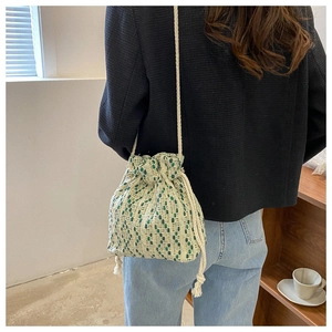 Detail of woven drawstring bucket bag with green and beige pattern on a female model