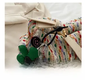 Detail of colorful woven tote bag featuring floral charm and white leather strap
