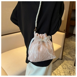 Close-up of pink pleated drawstring bucket bag featuring a large organza bow and pearl strap