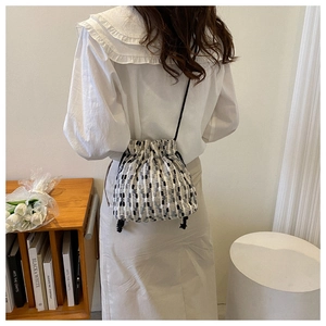 Detail of a woven drawstring bucket bag showing black and white texture and long strap