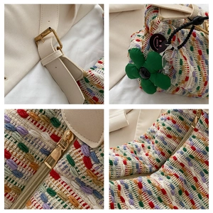 Detail view of colorful woven tote bag featuring gold zipper and green floral charm