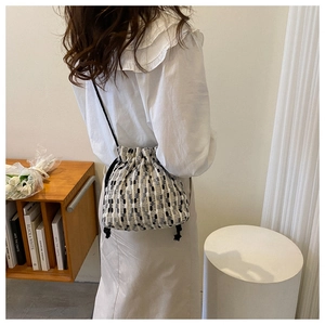Detail of tweed bucket bag with drawstring closure and slim strap on female model