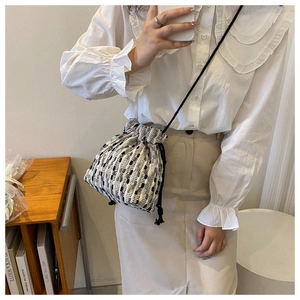 Detail of woven checkerboard bucket bag with drawstring strap on a model shoulder