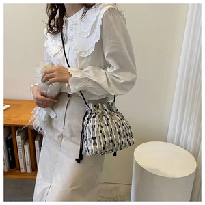 Detail of tweed drawstring bucket bag with black strap in a minimalist setting