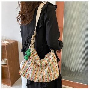 Colorful woven tote bag shown on shoulder with a sunflower charm in a lifestyle setting