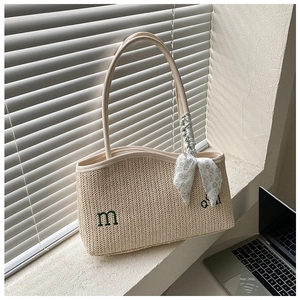 Detail of beige straw tote bag with green 'md' embroidery and floral silk scarf accessory