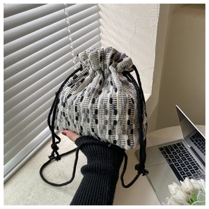 Detail of tweed drawstring bucket bag with black rope handles and woven texture