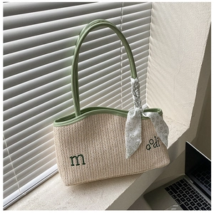 Detail of straw woven tote bag featuring green embroidery and floral scarf on handle