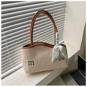 Detail of beige straw tote bag featuring green embroidery and a floral scarf handle