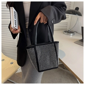 Detail shot of black bucket bag with silver rhinestones and rivets being held by a model