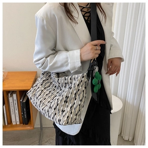 Close-up of woven shoulder bag with floral charm worn by a model in a cozy library