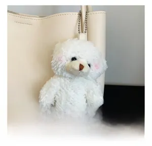 Close-up of white plush bear keychain with silver chain on an ivory tote bag