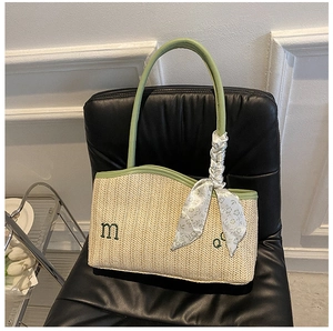 Detail of woven tote bag with green embroidery and silk scarf on a leather chair