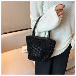 Close-up of sparkling black rhinestone bucket bag held by model wearing white sweater