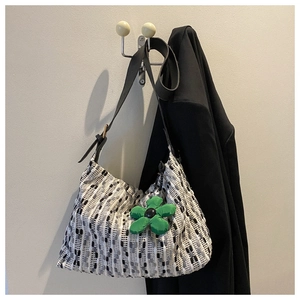 Detail of black and white woven tote bag with a green floral charm on a black strap
