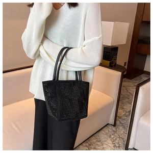 Detail of a chic black bucket bag with sparkling rhinestones held by a model in luxury room