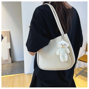 Close-up of minimalist cream white shoulder bag with cute plush bear charm detail