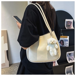 Detail of minimalist beige tote bag with a white plush bear charm and long shoulder strap