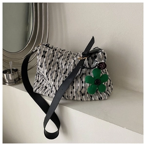 Detail of tweed woven shoulder bag with wide strap and a green flower plush pendant
