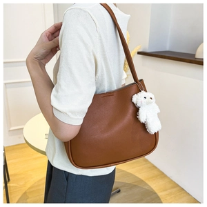 Detail of minimalist brown shoulder tote with a cute white teddy bear plush charm accessory