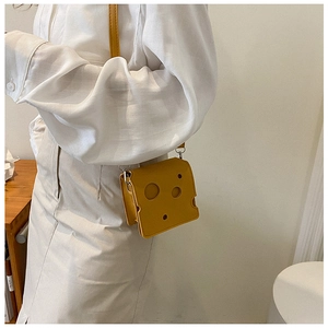 Detail of creative yellow cheese-shaped crossbody bag worn over a white shirt