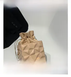 Detail view of beige quilted bucket bag featuring geometric texture and gold chain strap