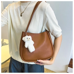 Detail view of a caramel brown faux leather tote bag with a white plush bear charm