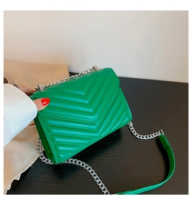 Detail of green quilted square crossbody bag with silver chain and V-shaped stitching