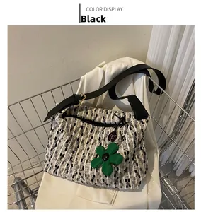 Detail of black tweed tote bag with green flower charm on a white fabric background