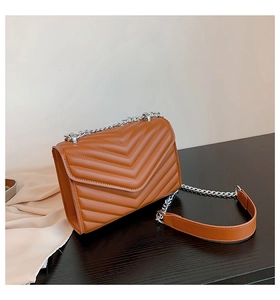 Close-up of brown quilted faux leather handbag with silver chain strap on wooden surface