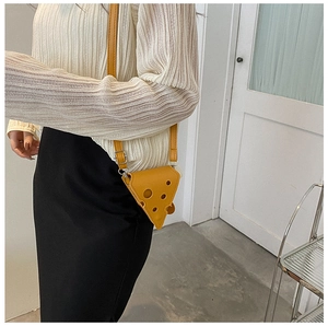 Close-up of yellow cheese-shaped mini crossbody bag worn with white pleated top and black skirt