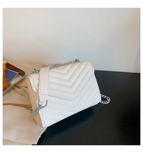 Detail of white quilted crossbody bag with chevron pattern and silver chain strap