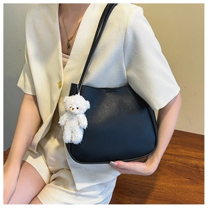Close-up of black leather tote bag with a cute white teddy bear charm accessory