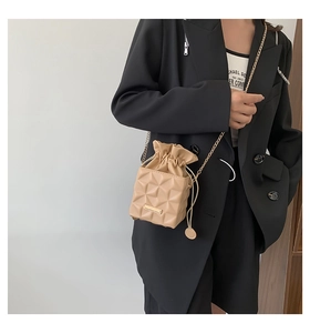 Detail of beige drawstring bucket bag with geometric texture and gold chain strap