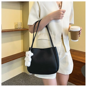 Detail of a large matte black leather tote bag with a white plush bear charm accessory