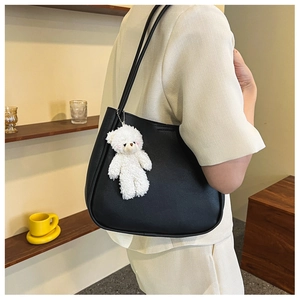 Close-up of black leather shoulder bag with a cute white plush bear pendant detail