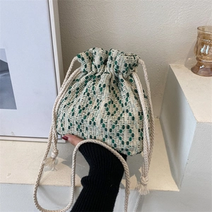 Green and white woven drawstring bucket bag with cotton rope strap in a minimalist setting