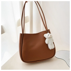 Detail of soft brown faux leather shoulder bag featuring a cute white teddy bear charm
