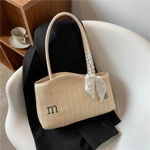 Large straw tote bag with green embroidery and floral scarf on a white chair